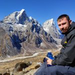 a man sitting in front of the panoramic view of mt. lobuche and chola che. pic for the testimonial