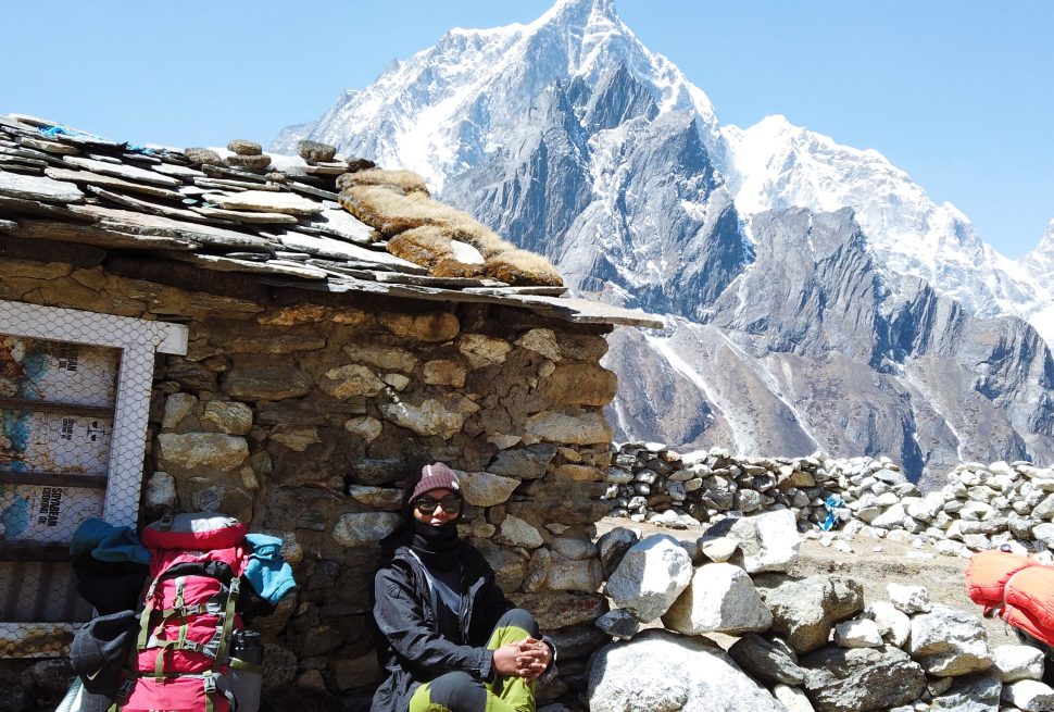 a woman stands in front of an abandoned house along the ebc trekking trail in dingboche, nepal.