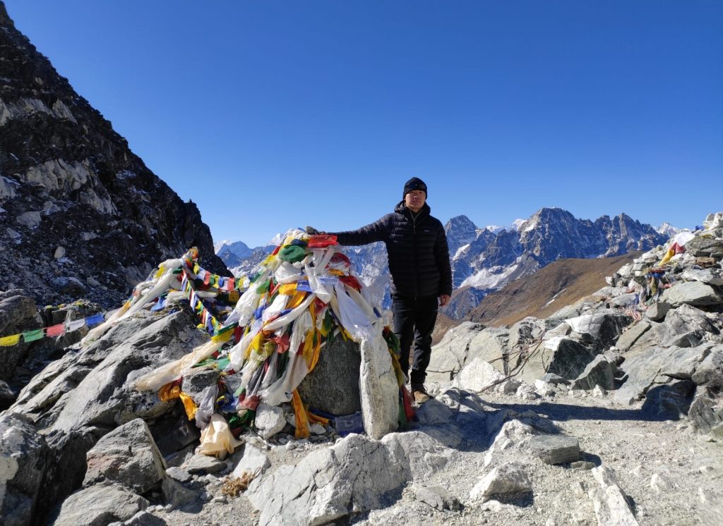 a man stands in front of a chaitya in the three pass trekking trail in front of the mountains.